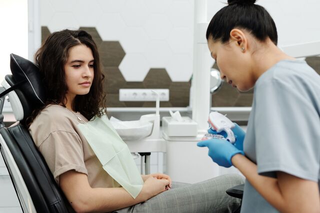 a woman sits in a dental chair while a dental professional wearing gloves shows her a dental model