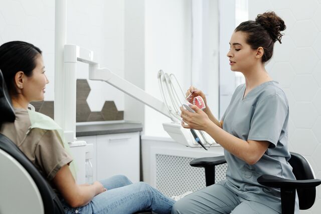 a woman relaxes in a dentist chair while a man talks to her likely discussing her dental care or treatment