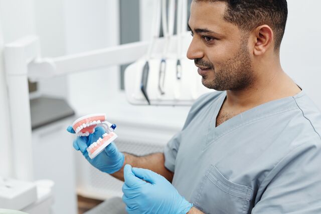 a man in a dental office holding a teeth model and looking at the camera with a friendly expression